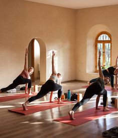 a group of people doing yoga poses in a room with wooden floors and arched windows