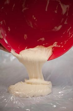 a red bowl is being filled with white batter on a sheet of plastic wrapper