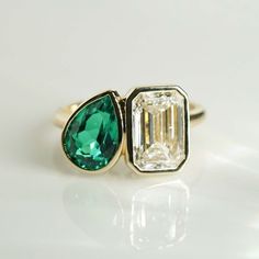 an emerald and diamond ring on a white surface