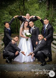 a bride and groom with their wedding party posing for a photo on a bridge in the woods