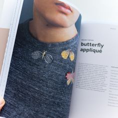 a person is holding an open book in their hand and looking at the page with butterfly applique on it