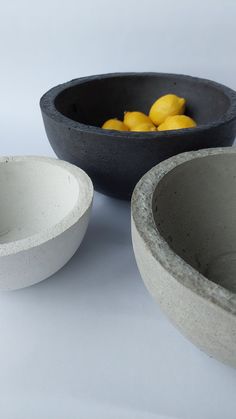 three cement bowls with lemons in them on a white tableclothed surface,