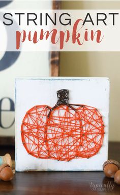 string art pumpkin sitting on top of a wooden table next to some acorns