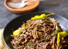 a black bowl filled with shredded meat and green peppers