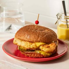 a chicken sandwich on a red plate next to a glass of orange juice and a jar of mustard