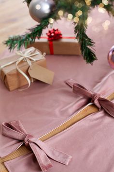 presents are wrapped in pink paper and tied with ribbon on a table next to a christmas tree