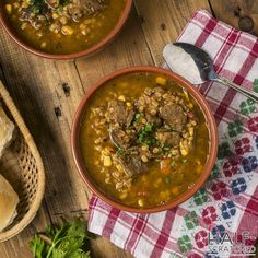 two bowls filled with soup sitting on top of a table next to bread and spoons