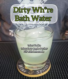 a glass filled with green liquid sitting on top of a black table next to a person