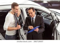 two men standing next to each other in front of a car and holding clipboards