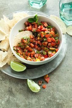 a white bowl filled with salsa next to tortilla chips and lime wedges