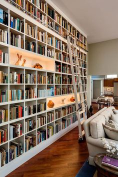 a living room filled with lots of books on top of a white book shelf next to a couch