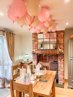 a dining room table with pink and white balloons hanging from it's ceiling in front of a brick fireplace