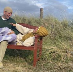 a man sitting on top of a wooden bench next to tall grass and sand dunes