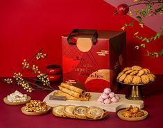 an assortment of snacks and desserts on a table with red wall in the background