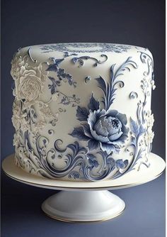 a blue and white cake with flowers on it's side, sitting on a pedestal