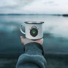 a person holding a white and black coffee cup with a green face on the front