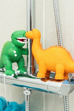 two toy dinosaurs are playing with each other in the shower faucet and water hose