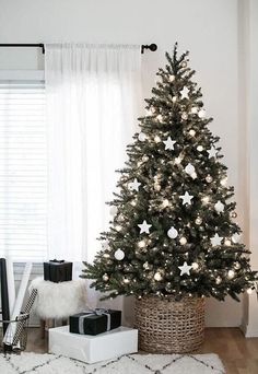 a decorated christmas tree in a living room with white curtains and presents on the floor