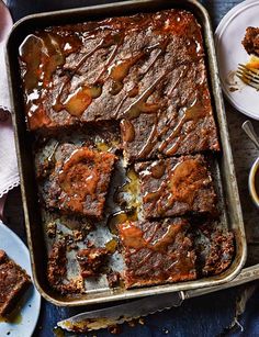 a pan filled with brownies next to two plates of desserts and utensils