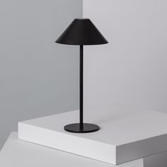 a black lamp sitting on top of a white table next to a gray and white wall