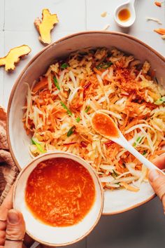 someone holding a spoon over a bowl of food with sauce in it and other ingredients around the bowl