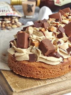 a cake with chocolate and peanut butter toppings on a cutting board next to nuts