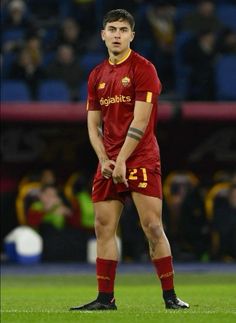 a man standing on top of a soccer field wearing a red uniform and black socks