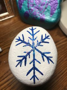 a painted rock sitting on top of a wooden table next to a purple and blue vase