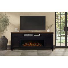 an entertainment center with a flat screen tv and fire in the fireplace, next to a large potted plant