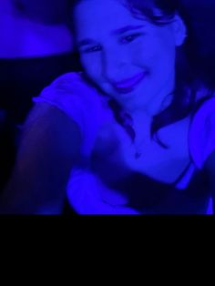 a woman is smiling and holding her cell phone up to the camera with blue light in the background