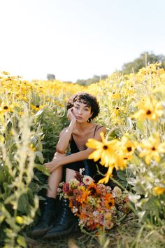 a woman sitting in the middle of a sunflower field with her hand on her face