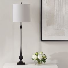 a white vase with flowers sitting on a table next to a black and white lamp