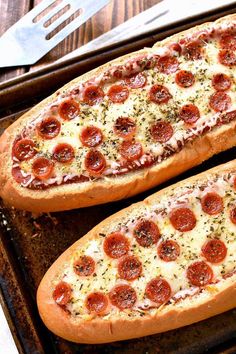 two pepperoni pizzas sitting on top of a baking pan next to a knife and fork