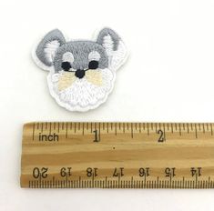 a wooden ruler with a small embroidered mouse on it next to a piece of wood