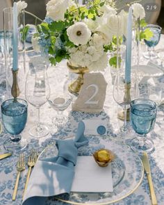 the table is set with blue and white linens, silverware, and flowers