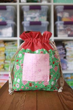 a green bag with a red bow sitting on top of a wooden table in front of shelves