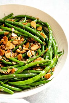 a white bowl filled with green beans and almonds on top of a marble table