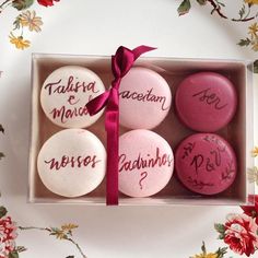 six pink and white buttons with writing on them in a gift box next to flowers