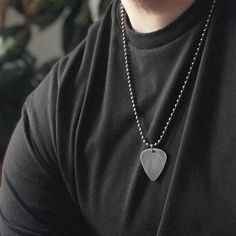 a man wearing a black t - shirt with a silver heart pendant on his neck