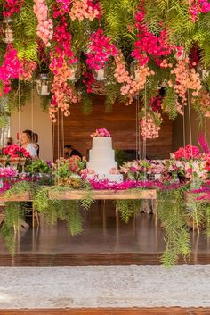 a wedding cake sitting on top of a wooden table surrounded by pink and green flowers