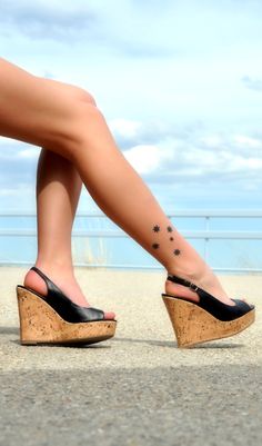 a woman's foot with a star tattoo on her left ankle and black wedges