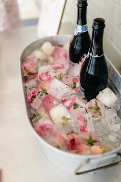 two bottles of champagne and ice in a bucket filled with flowers on a counter top