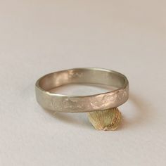 a close up of a silver ring on a white surface with a seashell in the foreground