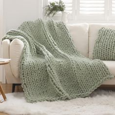 a white couch with a green blanket on top of it next to a table and potted plant