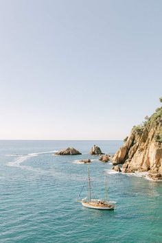 a small boat floating on top of the ocean next to a rocky cliff covered shore