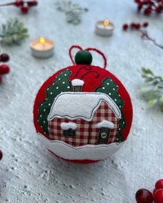 a red ornament with a white house on it and some candles in the background