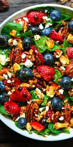 a salad with berries, blueberries, pecans and walnuts in a white bowl