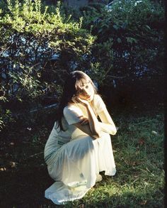 a woman is sitting in the grass with her hands on her face and looking down