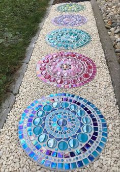 several different colored glass circles are on the side of a gravel path that is lined with stones