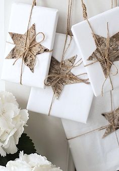 three wrapped presents tied with twine on top of each other next to white carnations